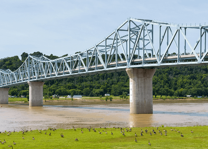 trussed bridge over water with birds on the grassy banks