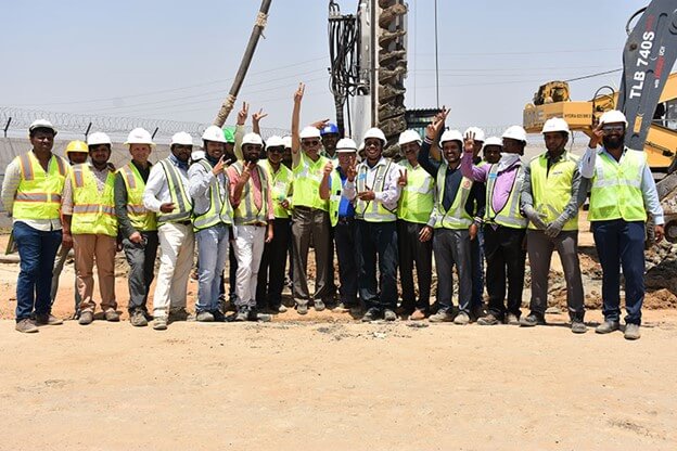 large group of men in construction gear with heavy machinery behind them